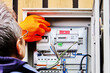 An electrician wearing protective dielectric gloves turns off power supply to circuit breaker in an external electrical panel.