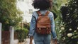 Rear view of slim African American teenage girl in jeans walking away, carrying brown leather backpack