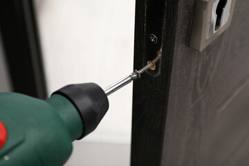 Poster - Handyman with electric screwdriver repairing door handle indoors, closeup