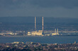 “Vista Industrial al Atardecer”. La foto captura una zona industrial con altas chimeneas destacando contra un vasto paisaje.