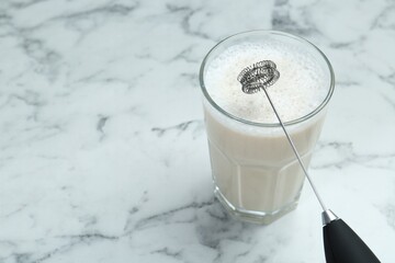 Mini mixer (milk frother) and tasty cappuccino in glass on white marble table, closeup. Space for text