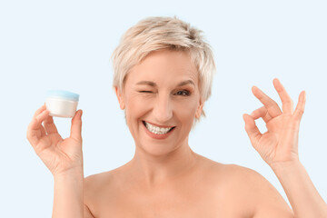 Canvas Print - Mature woman with jar of anti-aging cream showing OK on blue background, closeup