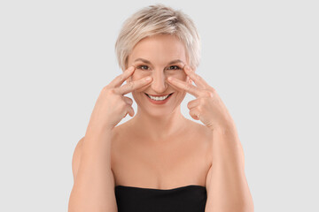 Sticker - Beautiful mature woman massaging face on light background, closeup