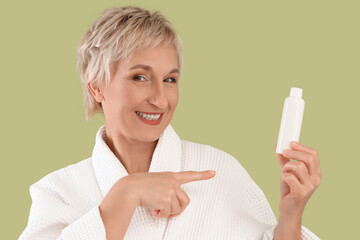 Poster - Mature woman pointing at bottle of skincare product on green background, closeup