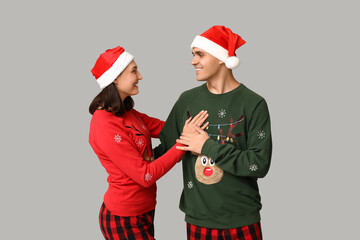 Wall Mural - Happy young couple in Christmas pajamas and Santa hats on grey background