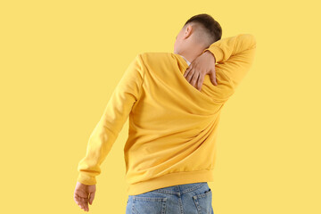 Wall Mural - Young man suffering from back pain on color background