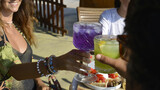 Fototapeta  - brindisi tra amici con cocktail colorati in un bar all'aperto in riva al mare