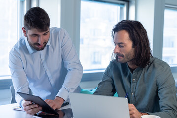 Poster - Travail en équipe. deux collègues travaillent ensemble dans un bureau sur le même projet. Ils discutent et sont assis devant un ordinateur portable.