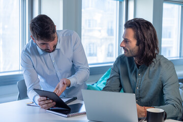 Poster - Travail en équipe. deux collègues travaillent ensemble dans un bureau sur le même projet. Ils discutent et sont assis devant un ordinateur portable.