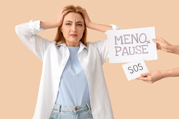 Wall Mural - Mature woman and hands holding papers with text MENOPAUSE SOS on beige background