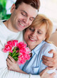Close up vertical portrait of young son hugging his smiling mother at home with bouquet of tulips. Birthday, Mother's day, women day, retired.