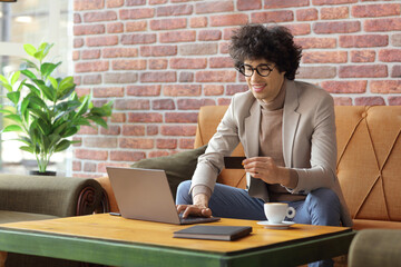 Sticker - Young man sitting in a cafe using a laptop computer and holding a credit card