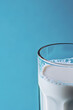 PART OF A GLASS GLASS, FILLED WITH PURE MILK ON A LIGHT BLUE BACKGROUND