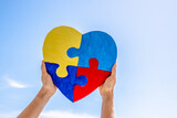 Fototapeta Mapy - World autism awareness day, Autism spectrum disorder concept. Adult and child hands holding together colorful painted puzzle heart on blue sky background