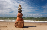 Fototapeta Na sufit - Stone zen pyramid made of colorful pebbles on the beach against a stormy sea.
