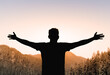 Young man arms outstretched on a mountain at sunrise enjoying freedom and life, people travel wellbeing concept
