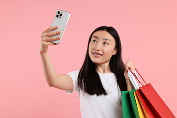 Poster - Smiling woman with shopping bags taking selfie on pink background