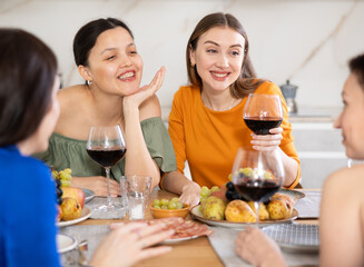 Wall Mural - Girlfriends chatting and drinking wine at home party table in kitchen