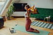 A woman is kneeling on a yoga mat in a plantfilled room, using an orange resistance band