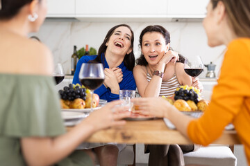 Wall Mural - Girlfriends chatting and drinking wine at home party table in kitchen