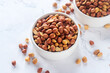 Roasted salted peanuts in white ceramic bowl on white marble background.