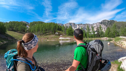 Wall Mural - Hiker couple at alpine lake with scenic view of mountain peaks Feistritzer Spitze (Hochpetzen) and Kriznik, Karawanks, Carinthia, Austria. Wanderlust Austrian Alps. Hiking trail on Petzen, Bleiburg