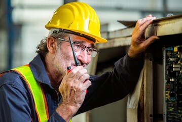 Wall Mural - man engineer technician worker talk call by use mobile radio walkie talkie communicate speak to service technician. worker in uniform helmet safety and inspection check control old machine in factory