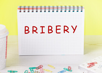 Wall Mural - Word BRIBERY written on a checkered notebook on a yellow background