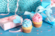 Delicious cupcakes with question mark, gift boxes and decorations on blue wooden table against white background. Gender reveal party concept