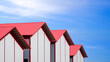 Row of cold storage warehouse buildings with white sandwich panel wall and red metal gable roof against blue sky in industrial settlement area, perspective side view