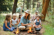 Mature adult woman, mother or kindergarten teacher, with 5 five children sitting on the ground, in the forest on a trip or camping, annoyed and stressed