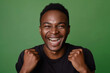 Handsome black man with short hair is smiling and celebrating his success on green background, dressed in casual. He has a happy expression after winning a game or getting good news from work