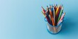 colored pencils in wire mesh cup on light blue background. Top view, space for text. Education, language learning, back to school concept