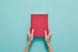 Woman hands holding book with blank red cover over light blue background. Education, back to school, self-learning, book swap, sharing, bookcrossing concept