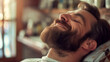 Happy man with a beard relaxing in a barber's chair, eyes closed, enjoying a haircut