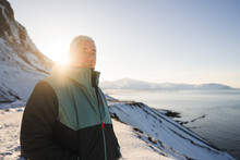 A traveler in a warm coat savors the tranquil moments of a sunlit winter day, overlooking the snowy coastline of Iceland