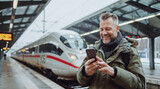 Fototapeta  - homme de 30-40 ans sur le quai d'une gare en train de consulter son smartphone en attendant son train