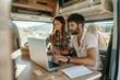 A young couple focused on their laptops inside a cozy camper van in nature