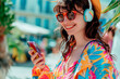 Smiling woman with headphones wearing colorful clothing using smartphone in the city, summer time