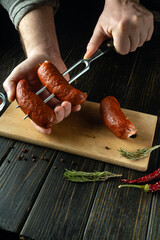 Preparing to cook a delicious grill with Czech sausages. A fork with sausages in the hands of a cook on the kitchen table. Advertising space