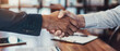 Two people shaking hands in front of a table with papers and a laptop by AI generated image
