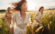 Portrait of cheerful smiling women friends clothed in light colors summer dresses walking by the high grass meadow sunset soft light shot. Woman's Friendship, relations and happiness concept imag