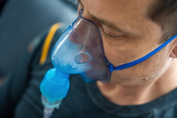 Close up view of unhealthy man wearing nebulizer mask in home. Health, medical equipment and people concept