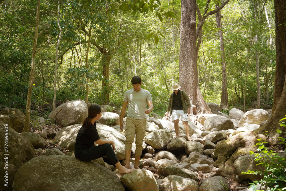 Group of three friends, one woman and two Asian men, hiking and sitting, camping, picnicking in the forest, having a stream and waterfall, relaxing during the weekend.Friendship and lifestyle