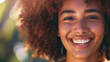 Close-up of a smiling woman with curly hair and freckles in sunlight