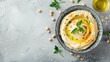 A bowl of creamy hummus topped with olive oil and herbs on a textured gray background