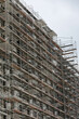 A multistory residential building under construction, enveloped in scaffolding, with a clear view of the work in progress against an overcast sky.