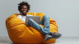 Fototapeta Sport - an African man smiling on a yellow sofa using a laptop