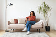 © Prostock-studio - Relaxing Afternoon at Home: Smiling Black Woman on Sofa in Living Room