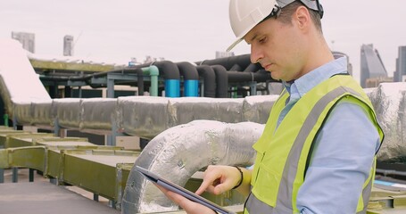 Canvas Print - Engineer inspecting insulated pipelines at an industrial site with a digital tablet.